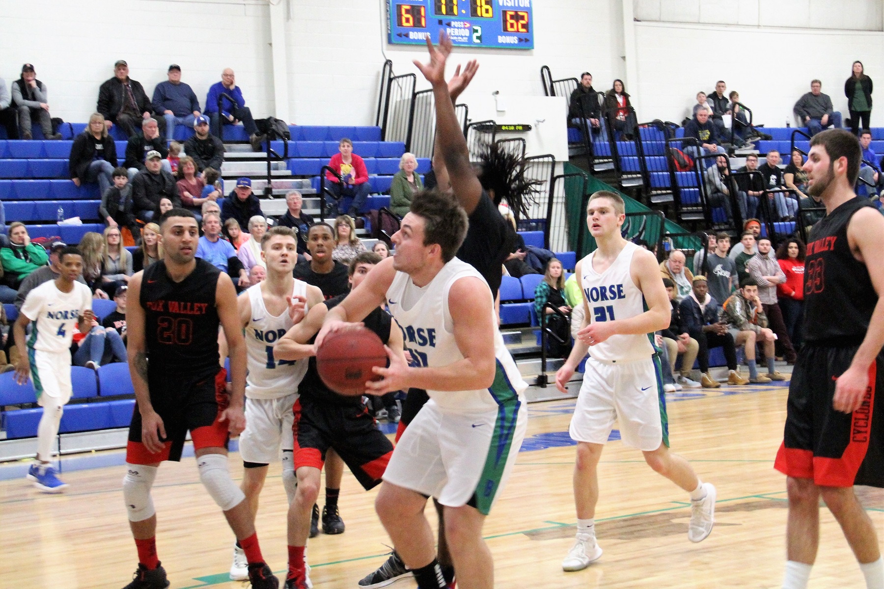 Damian Richmond going up for a shot underneath the basket, the defender behind him has an arm straight up in the air, a host of other players look on