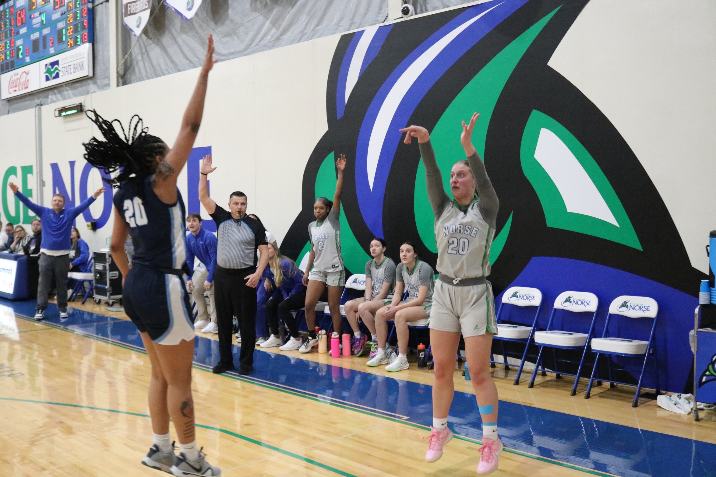Emma Rutter just after releasing a three-pointer in front of the Norse bench.  A defender is late in her attempt to block the shot.